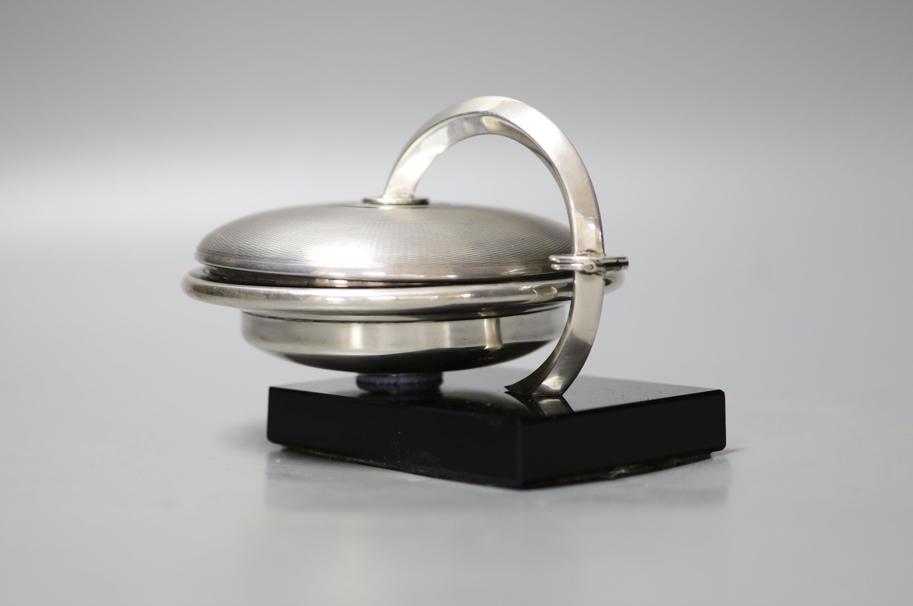 An unusual Art Deco engine turned silver and black enamel circular compact, with support arm, on black onyx? base (a.f.), Cohen & Charles, circa 1930, height 9.5cm.